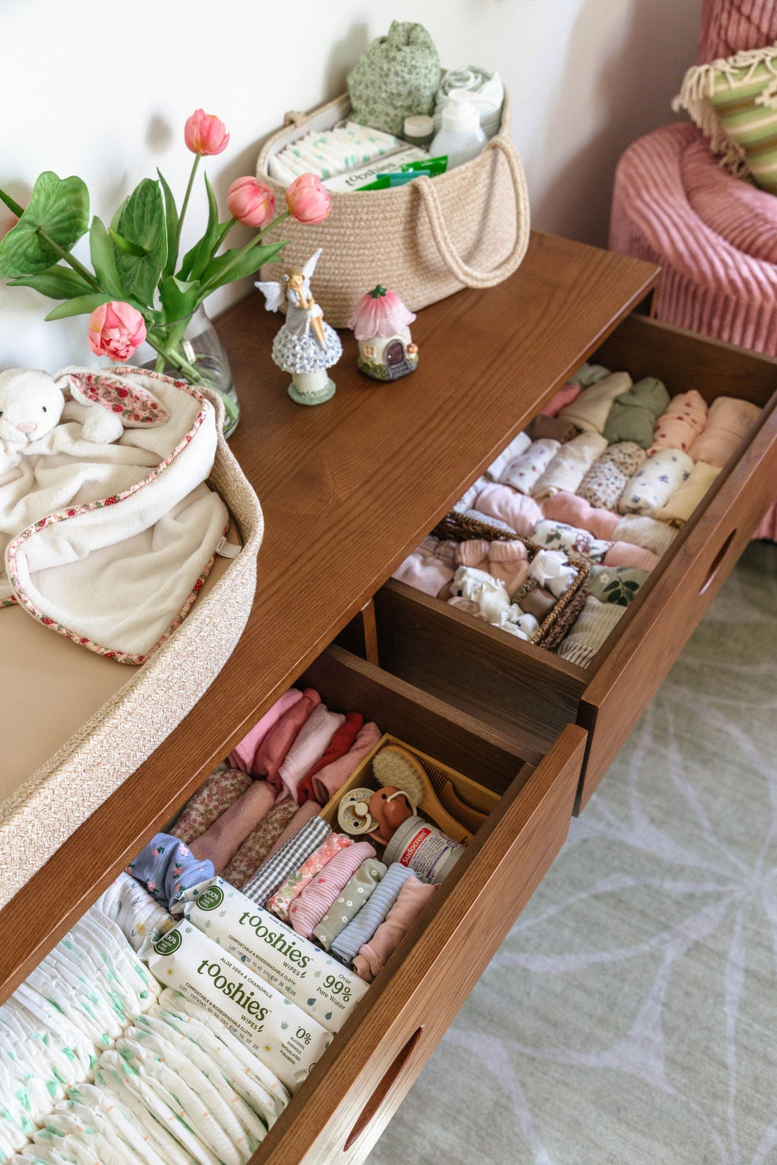 Neutral baby clothes shopping inspiration featuring a wooden drawer filled with neatly folded newborn outfits, soft baby blankets, knitted toys and natural accessories, perfect for a first baby clothes shopping list.