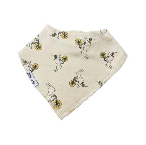 An off-white cotton bandana bib featuring a repeating pattern of cartoon rabbits carrying yellow and black shopping bags, with a small white brand tag reading 'Millie and Me' visible on one edge.