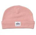A dusty pink knit beanie hat with a folded cuff, featuring a small white square patch on the front with a black embroidered logo.