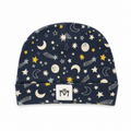 A navy blue baby beanie hat with a celestial print of stars, moons, and shooting stars, featuring a white fabric logo patch on the front cuff.