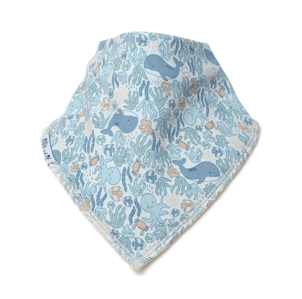A triangular baby bandana bib with a light blue and white ocean-themed print featuring whales, sea plants, and octopuses, finished with a soft cream-colored fringed edge.