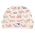 A baby beanie hat featuring a repeating pattern of stylised whales in muted pink, blue, and sage green on an off-white background. It has a folded cuff with a white square patch displaying a black logo.