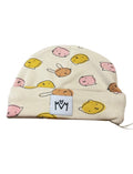 A cream-colored knit beanie hat featuring a playful pattern of cute cartoon faces in pink, yellow, and brown. A white fabric patch with a black logo stitched onto the front cuff.