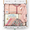 Curated baby gift box from Millie and Me featuring a pink striped romper, pink bunny comforter, baby book, bibs, hat and patterned baby accessories in branded tissue paper.