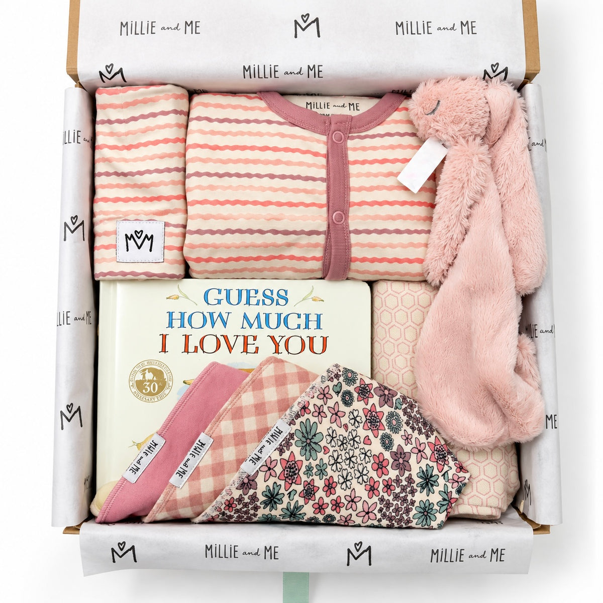 Curated baby gift box from Millie and Me featuring a pink striped romper, pink bunny comforter, baby book, bibs, hat and patterned baby accessories in branded tissue paper.