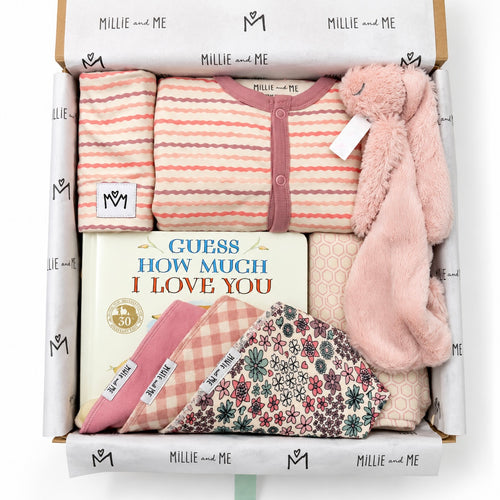 Curated baby gift box from Millie and Me featuring a pink striped romper, pink bunny comforter, baby book, bibs, hat and patterned baby accessories in branded tissue paper.