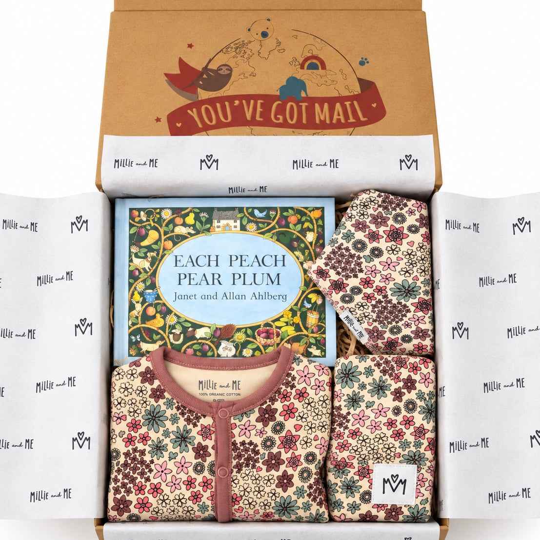A curated gift box set from Millie and Me, featuring a children's book titled 'Each Peach Pear Plum' surrounded by matching floral-patterned baby clothes and accessories, all arranged inside an open kraft paper box with branded tissue paper.