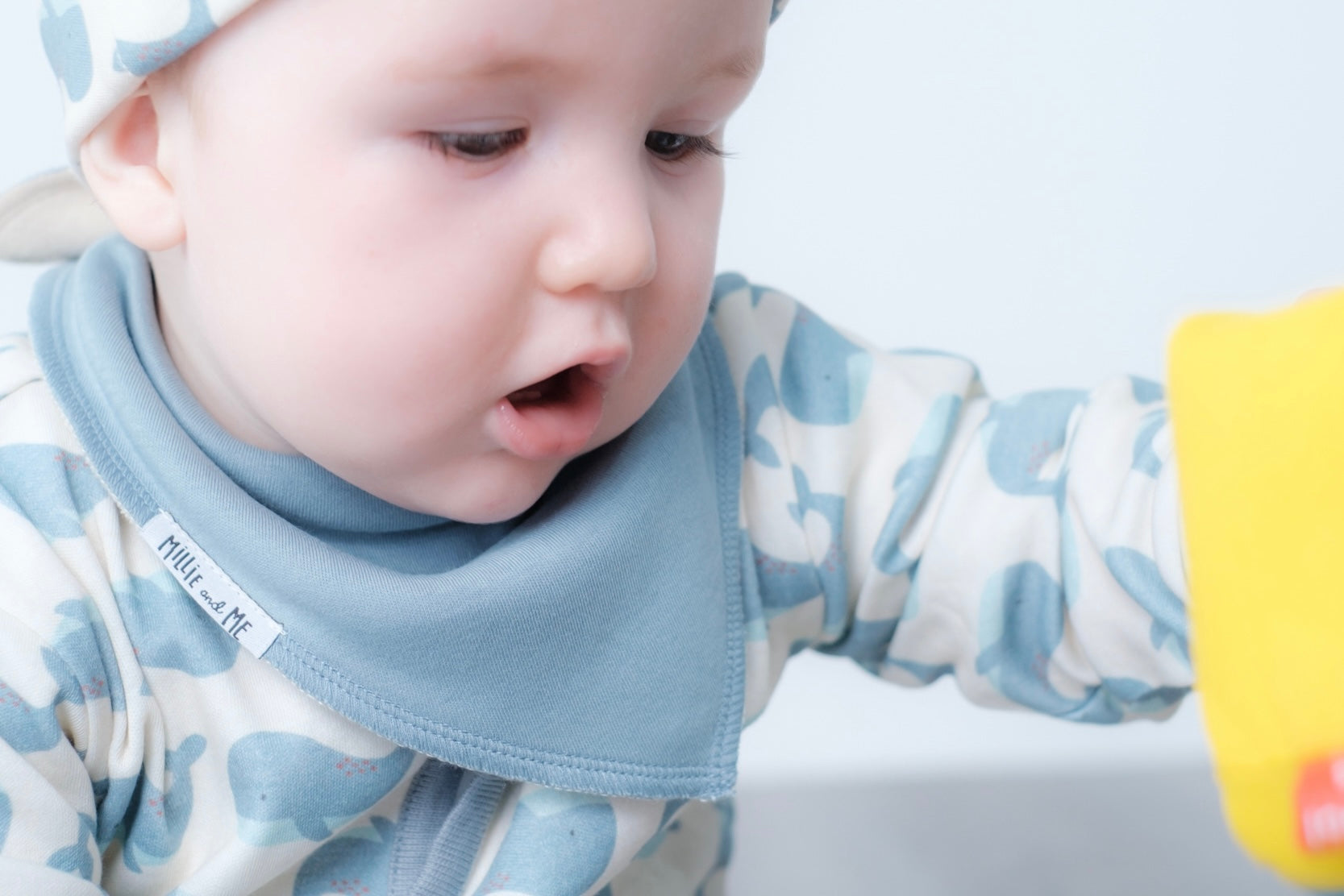 A close-up of a baby wearing a light blue bib and a matching blue and white camouflage long-sleeve top, looking down with a curious expression.