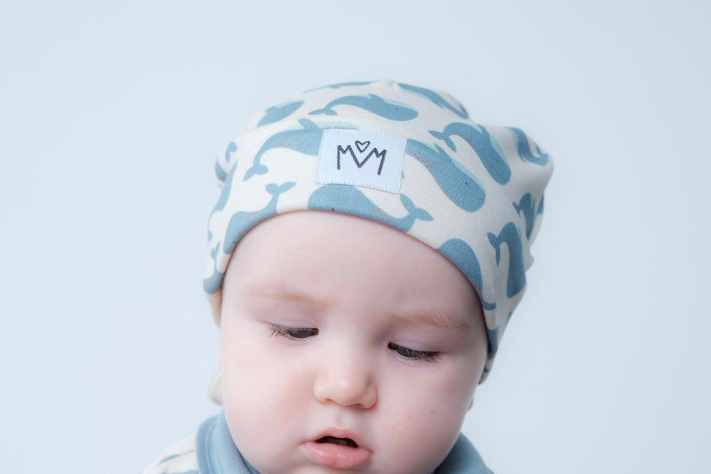 A beanie hat with a folded cuff, featuring a small white square patch on the front with a black embroidered logo.
