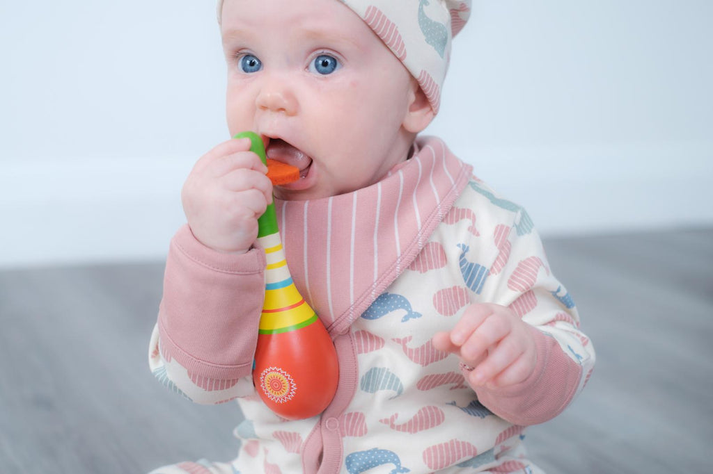 A baby wearing a pink and blue patterned long-sleeve romper, matching beanie hat, and a pink striped bib.