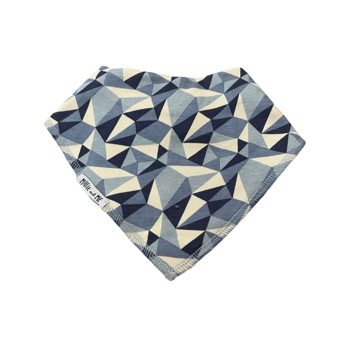 A triangular bandana bib with a geometric triangle pattern in navy blue, slate blue, and cream, featuring a visible 'Millie and Me' brand label on the side.