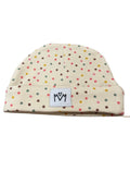 A cream-colored knit beanie hat with a multicolor polka dot pattern and a white brand patch on the front cuff.