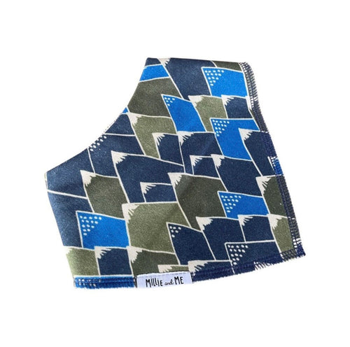 A fabric bib or pocket square featuring a geometric pattern of blue, navy, and olive green shapes outlined in white, with a small white label reading 'Millie and Me' at the bottom edge.
