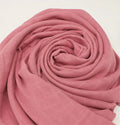 A dusty rose pink scarf or shawl draped in a neat spiral pattern, showing its soft, textured fabric, set against a plain off-white background.