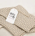 Folded beige fabric garment with a repeating blue geometric hexagon pattern, shown with a white paper tag reading Millie and Me.