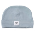 A light blue knit baby beanie hat with a folded cuff, featuring a small white square patch on the front with a black embroidered logo.