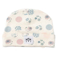 An off-white knit baby beanie hat featuring a delicate floral and polka dot pattern in dusty pink, light blue, and sage green. A white fabric patch with a black embroidered logo sewn onto the folded cuff.
