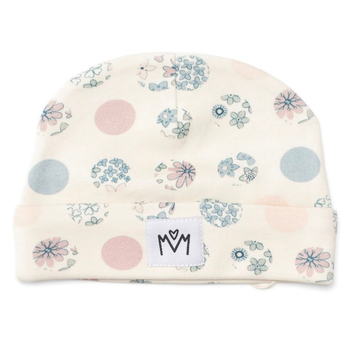 An off-white knit baby beanie hat featuring a delicate floral and polka dot pattern in dusty pink, light blue, and sage green. A white fabric patch with a black embroidered logo sewn onto the folded cuff.