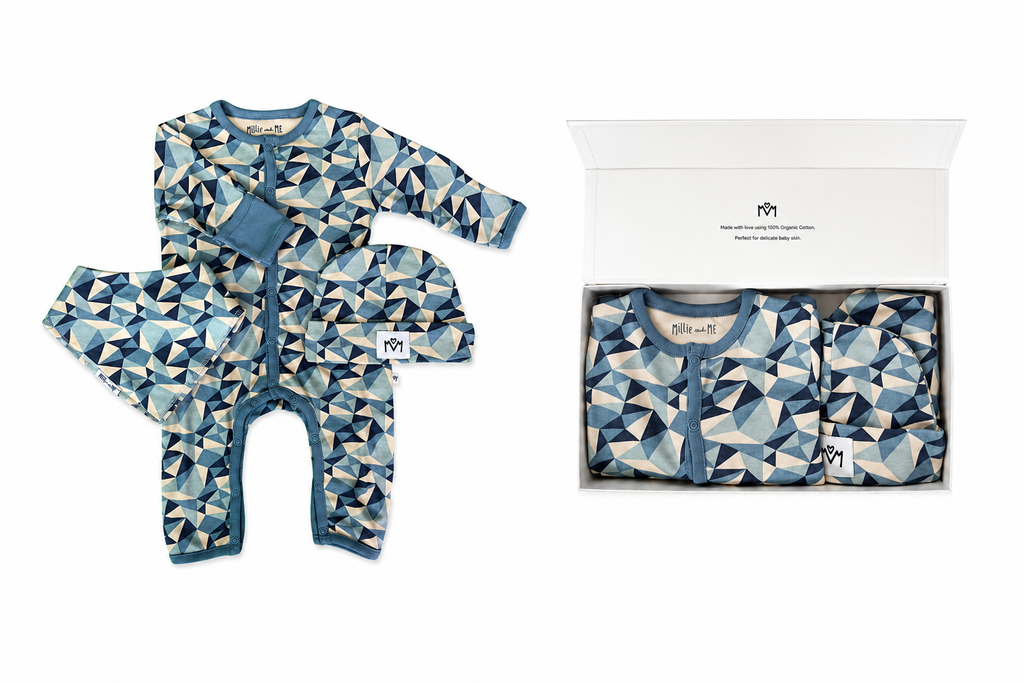 A baby long-sleeve footless romper with a geometric triangle pattern in shades of blue, navy, and beige, shown both laid flat and folded inside an open white gift box. The brand name 'Millie and Me' is visible on the inner neck label and inside the box.