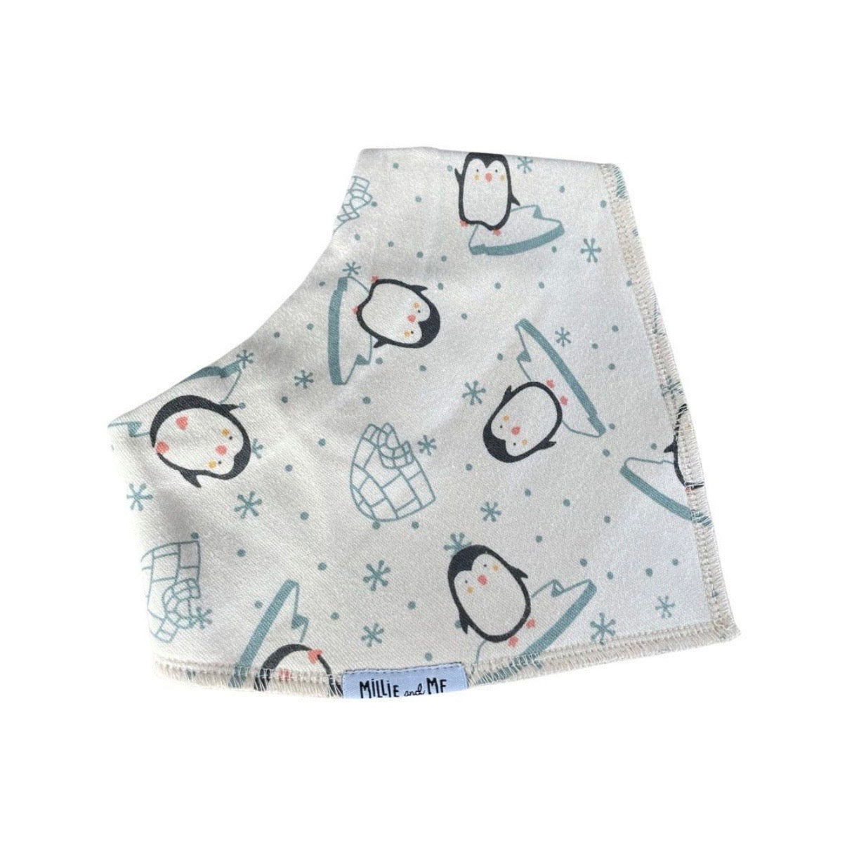 A square baby bib or bandana-style cloth with a winter penguin print, featuring black and white penguins, light blue icebergs, and snowflakes on a white background. A small white fabric tag at the bottom edge reads 'Millie and Me'.