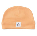 A peach-colored knit beanie hat with a folded cuff and a small white square patch featuring a black hand-drawn logo, shown on a plain white background.