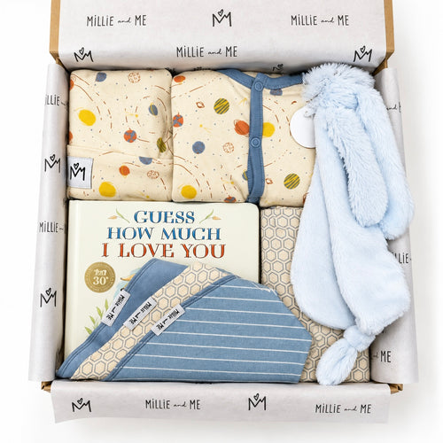 Curated baby gift box from Millie and Me featuring a blue romper, pink bunny toy, baby book, bibs, hat and patterned baby accessories in branded tissue paper.