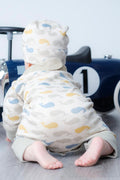 A baby crawling on a grey floor, wearing a cream-coloured hooded jumpsuit with a whale pattern in blue, yellow, and grey. The baby is positioned in front of a blue toy car.