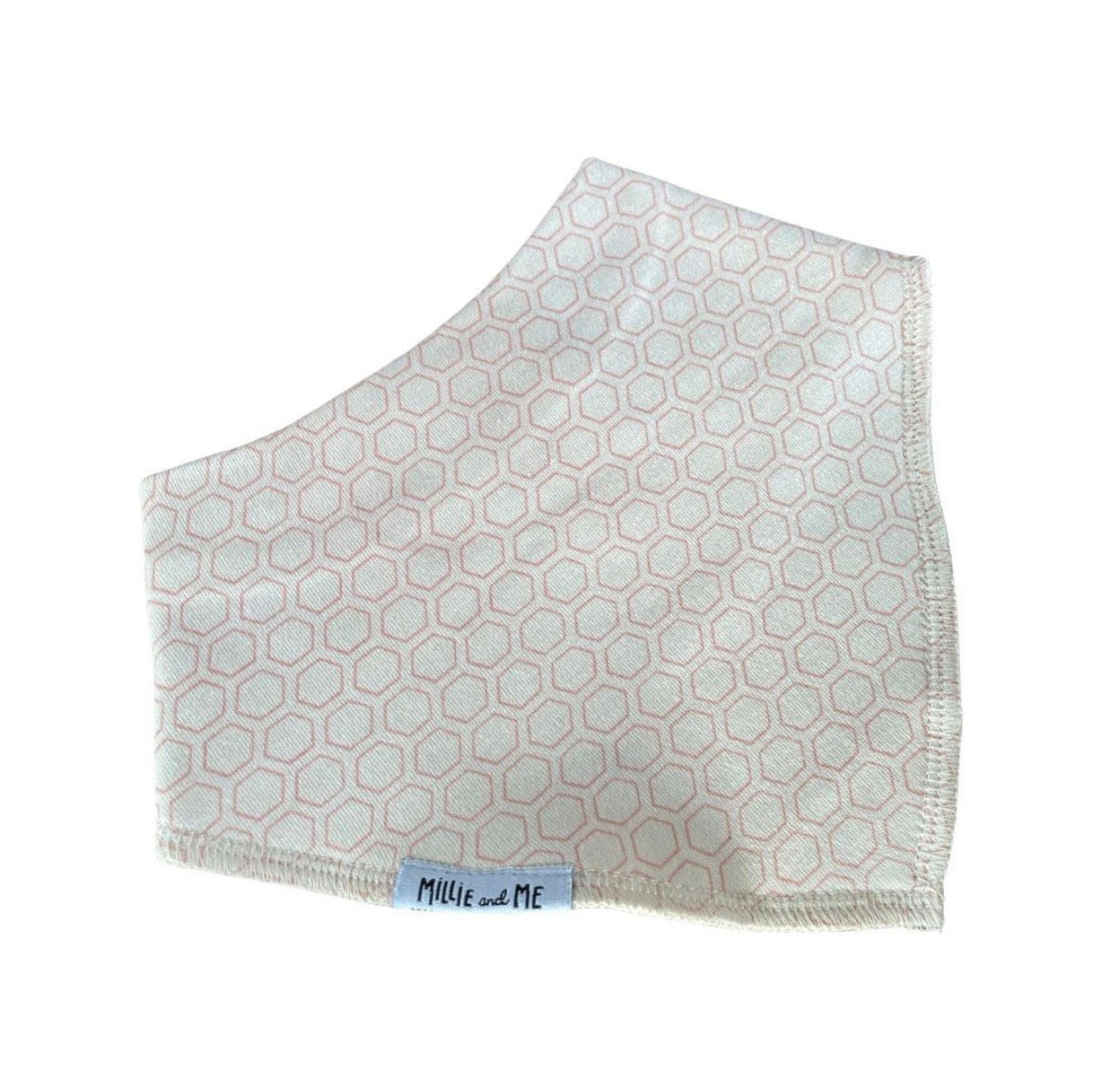 A square baby face mask made of soft cotton fabric, featuring a light pink and white geometric hexagon pattern and a small blue brand label reading 'Millie and Me' near the bottom edge.