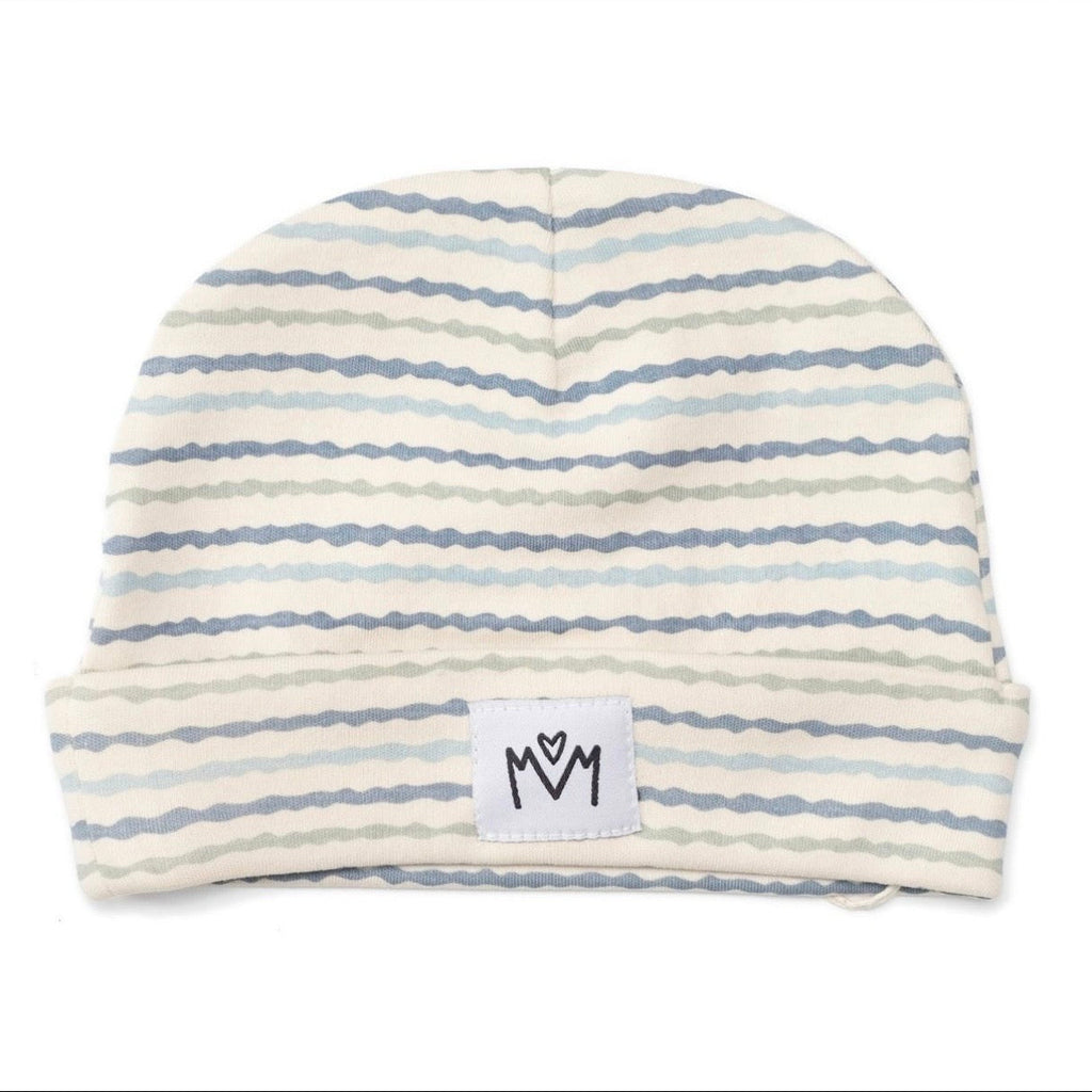A baby beanie hat with horizontal wavy stripes in light blue, gray, and beige on an off-white background, featuring a white brand patch with a black hand-drawn logo on the front cuff.