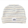 A baby beanie hat with horizontal wavy stripes in light blue, gray, and beige on an off-white background, featuring a white brand patch with a black hand-drawn logo on the front cuff.
