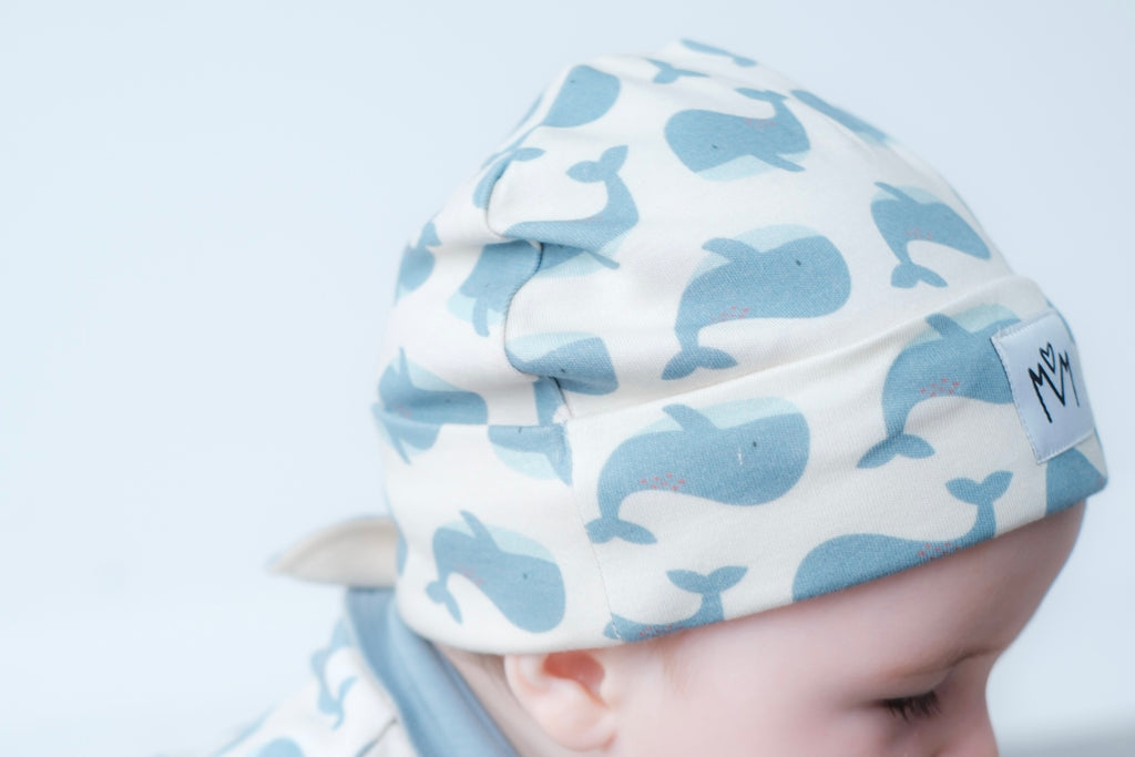 A beanie hat with a folded cuff, featuring a small white square patch on the front with a black embroidered logo.