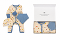A baby gift set featuring a cream-colored one-piece romper with multicolor polka dots, blue trim, a matching blue striped bib, and a matching beanie, shown both flat and inside its white gift box.