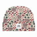 A folded knit beanie hat featuring an all-over dense floral and botanical pattern in pink, green, purple, and black on a light cream background. A small white rectangular brand patch with the stylised 'M M' logo is stitched onto the front fold.