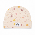 A beige knit beanie hat featuring a playful outer-space print with planets, stars, and curved lines in pink, yellow, and brown. It has a folded cuff with a white fabric patch displaying the stylized 'MM' brand logo.