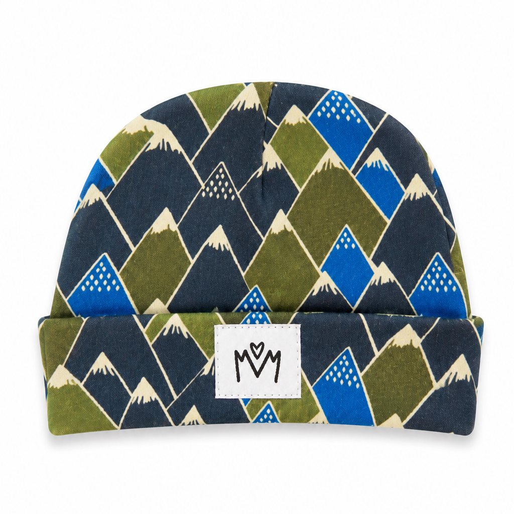 A folded knit beanie hat featuring a geometric mountain pattern in navy blue, olive green, bright blue, and cream, with a white fabric brand patch on the cuff.