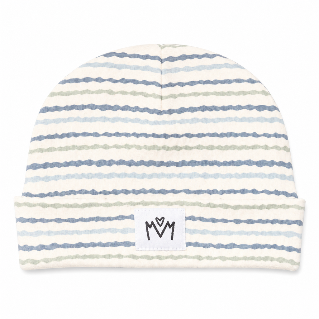 A knit beanie hat with horizontal wavy stripes in light blue, dusty blue, and sage green on an off-white background. It features a folded cuff with a small white square patch displaying a black stylized 'M' logo.