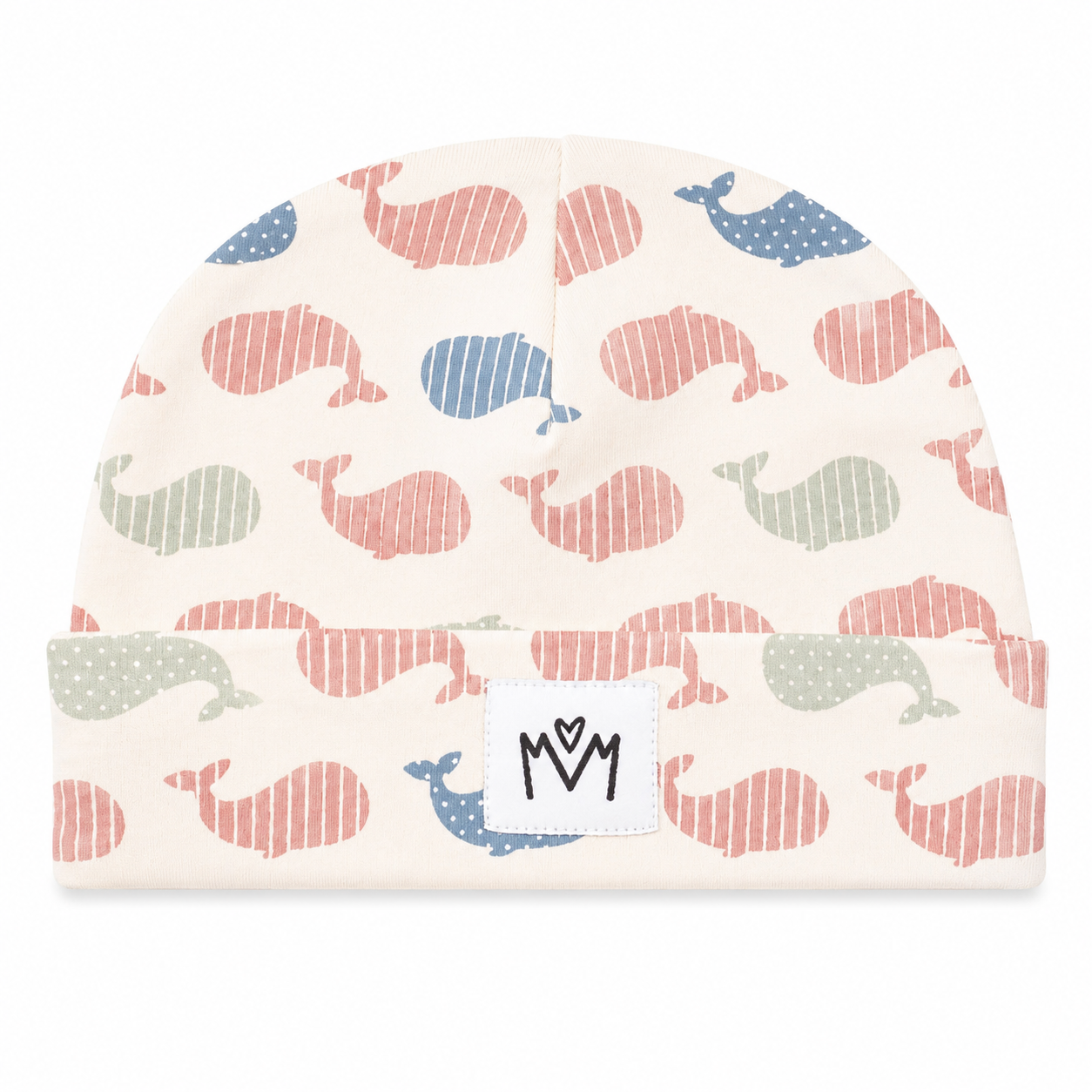 A baby beanie hat with an all-over whale print in muted coral, blue, sage green, and gray on a warm cream background. The hat has a folded cuff with a white square patch featuring a black stylized 'M' logo.