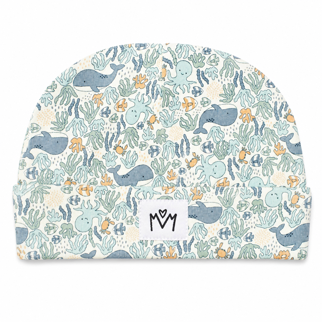 A baby beanie hat featuring an all-over underwater pattern with whales, octopus, fish, and sea plants in muted blue, teal, and orange on a cream background. A white fabric label with a black stylized 'M' logo is sewn onto the front.