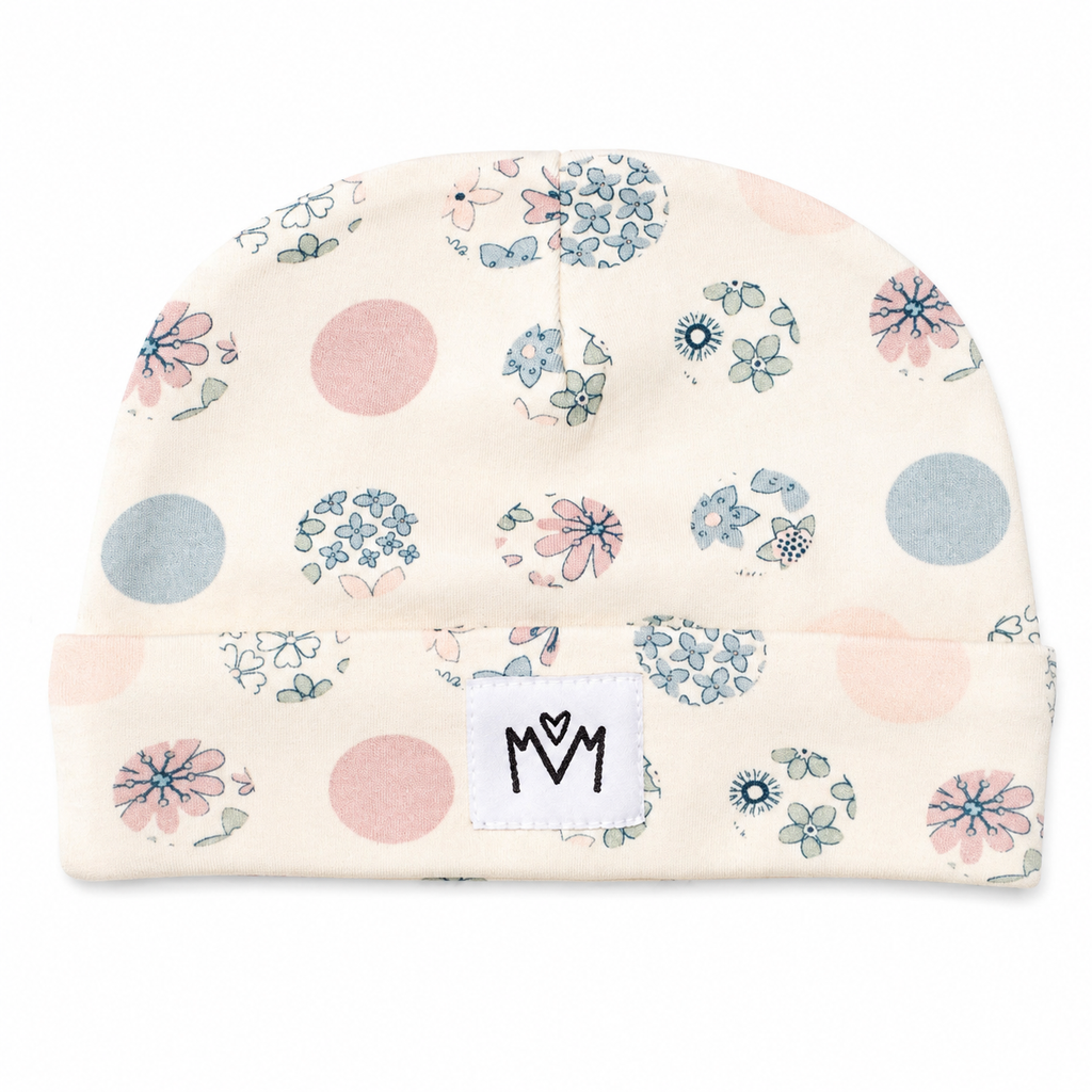 A cream-coloured knit beanie hat with a blue and pink floral pattern, a matching bib, and a small white patch that says 'MM' in black letters.