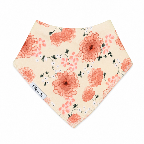 A triangular bandana bib with a floral print on a cream background, featuring coral-pink roses, green leaves, and small white blossoms. A white fabric tag on the left side reads 'Mille and Me'.