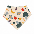 A triangular bandana bib with a cream background and a colorful print of fruits and vegetables, including avocado, banana, apple, carrot, and broccoli. A white fabric tag on the left side reads 'Millie and Me'.