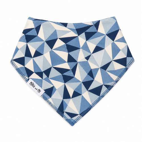 A triangular bandana bib with a geometric triangle pattern in shades of blue, navy, and cream, featuring a white fabric label that reads 'Millie and Me'.