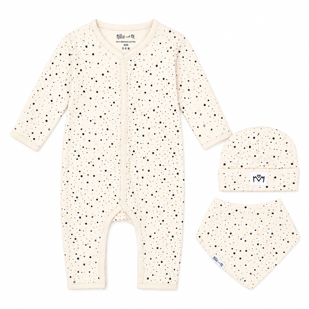 A three-piece baby clothing set including a long-sleeve footless romper, a beanie, and a bandana bib, all in an off-white/cream colour with a small black speckled pattern. The brand name 'Millie and Me' is visible on the inner neck label and on the beanie.