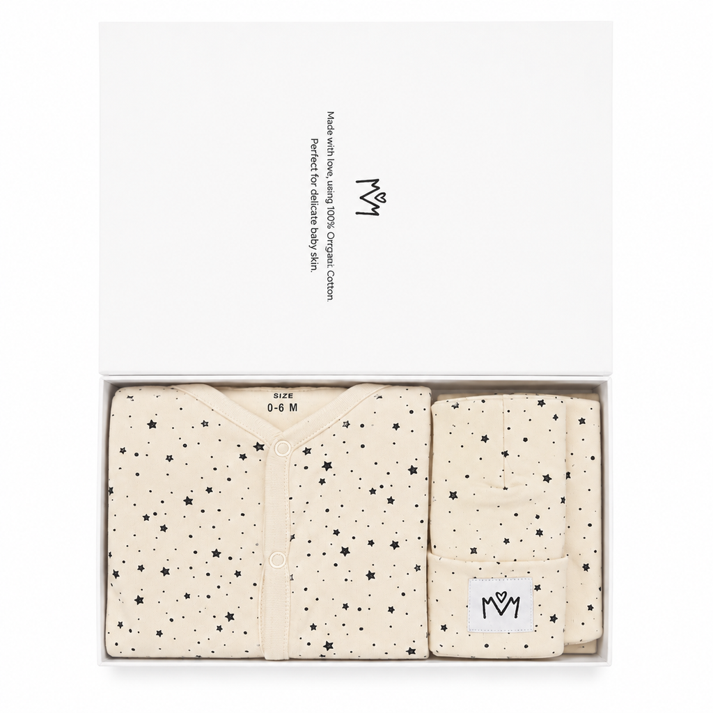 A baby gift set in a white box, featuring a cream-coloured baby cardigan and matching swaddle blanket with black star patterns. The brand logo 'MM' is visible on the packaging and the hat.