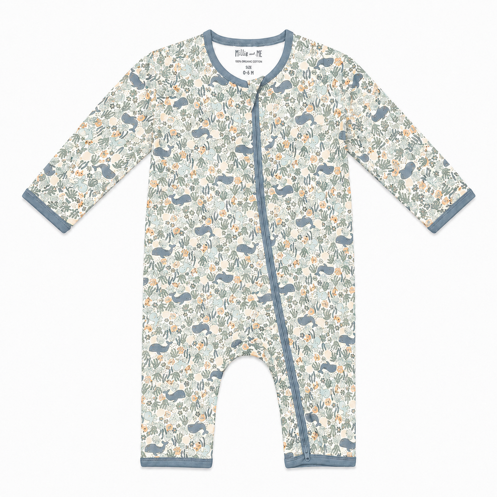 A baby long-sleeve footless one-piece sleeper with an ocean print featuring blue-gray whales, blue-gray fish, and orange accents on a cream background, with blue-gray trim.