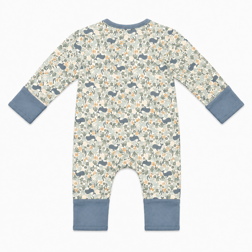 A baby long-sleeve footless one-piece romper with an ocean animal print featuring whales, fish, and corals on a cream background, finished with solid dusty blue cuffs and leg bands.