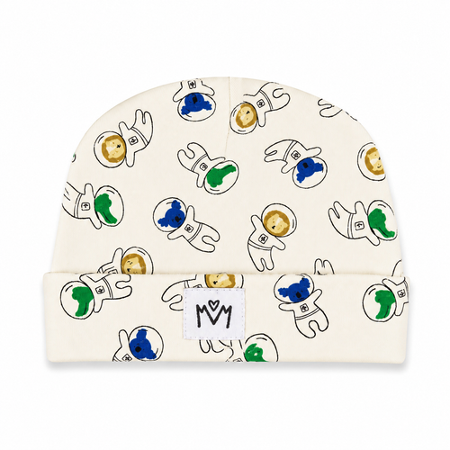 An off-white knit baby beanie featuring a playful pattern of cartoon astronauts in black outlines with blue, green, and gold accents. A small white fabric patch with a black 'MM' logo is sewn onto the folded cuff.