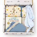 Curated baby gift box from Millie and Me featuring a blue romper, pink bunny toy, baby book, bibs, hat and patterned baby accessories in branded tissue paper.