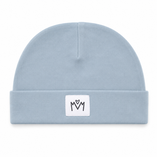 A light blue knit beanie hat with a folded cuff, featuring a small white square patch on the front with a black embroidered 'M' logo.