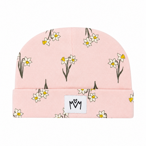 A light pink knit beanie hat featuring a repeating pattern of white daffodils with yellow centers and dark stems, with a white rectangular patch on the front displaying a black stylized 'MM' logo.